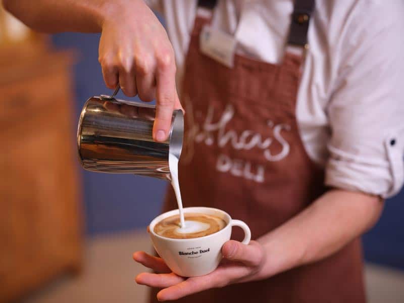 Een mannelijke barista schenkt melk in kopje met espresso om een cappuccino te maken